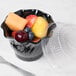 A black Cambro polycarbonate swirl bowl filled with fruit on a hospital cafeteria counter.
