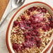 A bowl of oatmeal with whole and pieces of raspberries and a spoon.