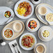 A table set with Acopa Foundations tan narrow rim melamine plates, bowls, and cups of food.