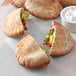 A plate with a small pita bread and a pita bread with vegetables inside, with a bowl of dip.