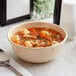 A tan Acopa Foundations melamine bowl of soup with a spoon.