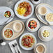 A table with Acopa Foundations white melamine plates, bowls of food, and utensils.