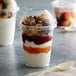 A Fabri-Kal Greenware plastic parfait cup filled with yogurt, fruit, and granola with a dome lid.