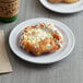 A pastry with white frosting on an Acopa Foundations white melamine plate on a table in a bakery display.