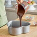 A heart-shaped anodized aluminum cake pan being filled with chocolate batter.