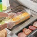 A person using a Vigor clear plastic food pan to serve food.