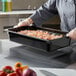 A chef holding a black Vigor food pan with vegetables.