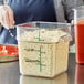 A person pouring cheese into a Vigor polycarbonate food storage container on a counter.