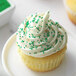 A cupcake with white frosting and green nonpareils.