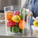 A woman cutting a yellow bell pepper in a Vigor clear square food storage container on a kitchen counter.