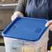 A person wearing blue plastic gloves holding a blue Vigor polypropylene food storage container lid over a blue plastic container.