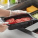 A person in gloves holding a Vigor black polycarbonate food pan with tomatoes.