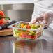 A person in gloves holding a Vigor 1/6 size clear polycarbonate food pan filled with food.