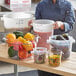 A woman holding a large clear round plastic food storage container full of vegetables.