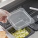 A person's gloved hand using a Vigor clear plastic lid to cover food in a clear plastic container.