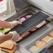 A person putting food into a black rectangular polycarbonate food pan lid.