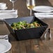 An Acopa Rittenhouse black square melamine bowl filled with salad on a table.