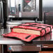 An American Metalcraft red nylon pizza delivery bag holding a pizza box on a stainless steel counter.