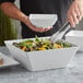 A person holding a white bowl of salad.