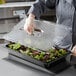 A person using a Vigor clear polycarbonate food pan lid with a handle to cover a tray of salad at a salad bar.