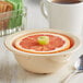 A tan melamine bowl with a slice of grapefruit on top and a spoon.