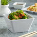 A bowl of food with broccoli, green onions and chopsticks on a table.