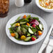 An Acopa white melamine plate with salad on a wood table.