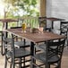 A Lancaster Table & Seating rectangular table with a textured walnut finish, chairs, a drink, and a potted plant on it.