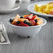 A white Acopa melamine bowl filled with fruit on a table.