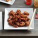 A plate of food on a table with an Acopa Rittenhouse white square melamine plate.