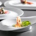 A Corona by GET Enterprises bright white porcelain plate with shrimp and a garnish on it.