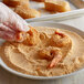 A gloved hand holding a shrimp being dipped into a bowl of J.O. Southern Fish Fry.