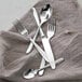 A group of Fortessa Grand City stainless steel spoons with silverware on a napkin.