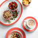 A stack of coral porcelain tea cups filled with coffee on a table with a plate of fruit and nuts.