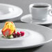 A Corona by GET Enterprises bright white porcelain plate with a slice of fruit on it and a cup of coffee.