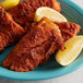 A plate of fried fish with lemon wedges on a white plate.