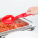 A hand using a Cambro red plastic salad bar spoon to serve food.