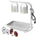 An Avantco silver countertop heat lamp with two red bulbs over a tray and wire grate.