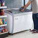 A man opening the curved glass door of an Avantco ice cream freezer.