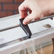 A person using a Bulman counter mount food wrap film dispenser to cover a piece of metal with plastic wrap.