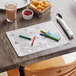 A wooden table set with food and a Choice Kids Dinosaur Interactive Placemat with crayons.