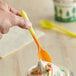 A hand holding a yellow to orange color-changing dessert spoon over a cup of ice cream.