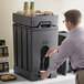 A man using a Cambro insulated beverage dispenser to pour water.