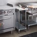 A Regency stainless steel filler table with backsplash and galvanized undershelf on a counter in a kitchen with stainless steel appliances.