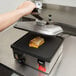 A person using a Vollrath Cayenne Single Panini Sandwich Press to grill a sandwich.