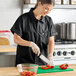 A woman in a Uncommon Chef black cook shirt cutting peppers.