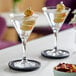 Two Schott Zwiesel martini glasses with olives on a table.