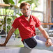 A man sitting on a bench wearing a red Uncommon Chef cook shirt.