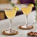 Two Schott Zwiesel Nick and Nora glasses of yellow liquid with lemon wedges on a table.