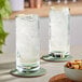 Two Schott Zwiesel beverage glasses of water with ice on a table with a bowl of nuts.